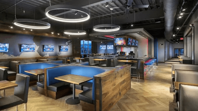 Interior of a Topgolf venue featuring modern furnishings, multiple seating areas, and large screens displaying sports.